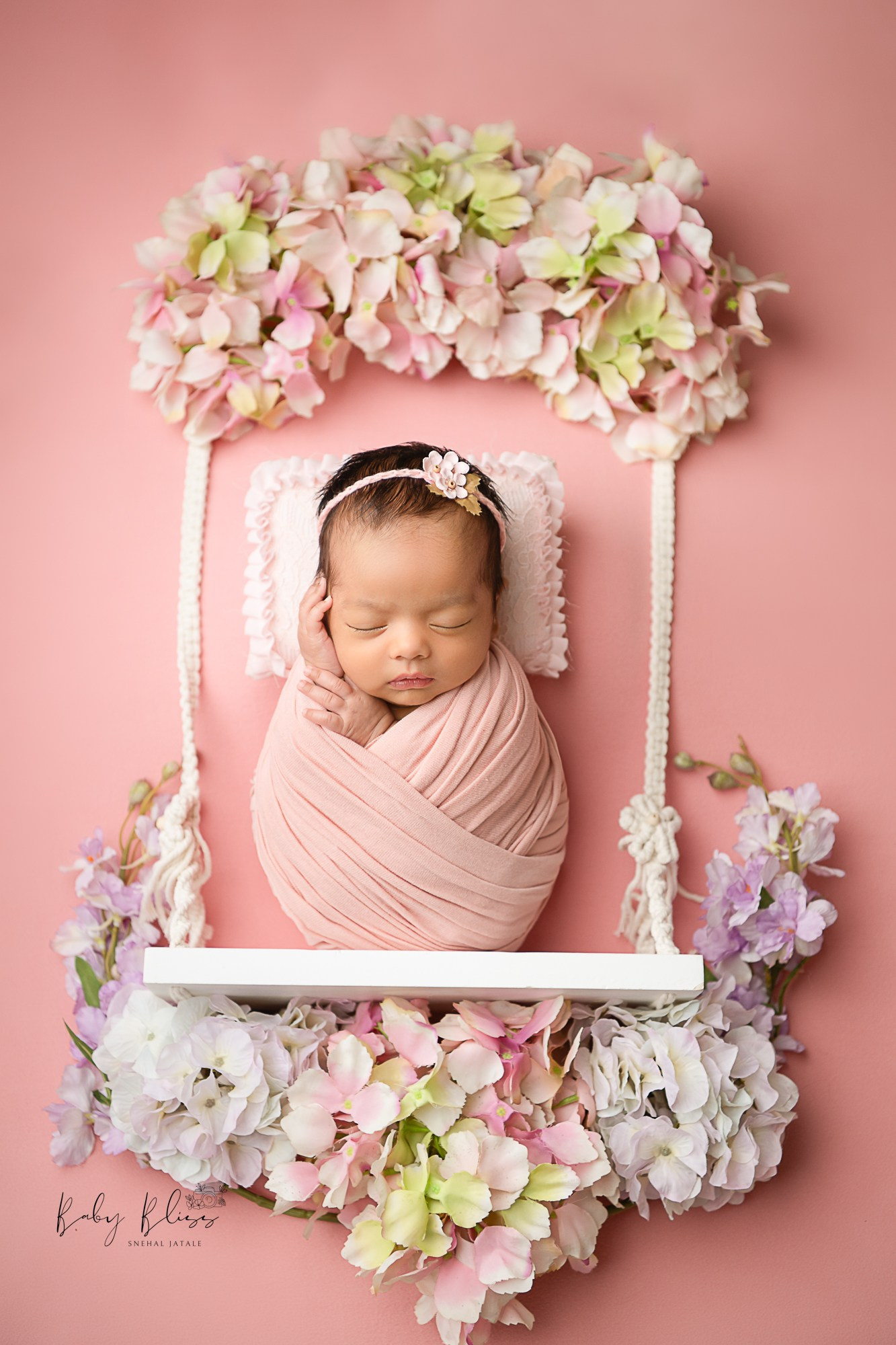 beautiful floral setup in light pink colour where little baby is wrapped and sleeping peacefully.