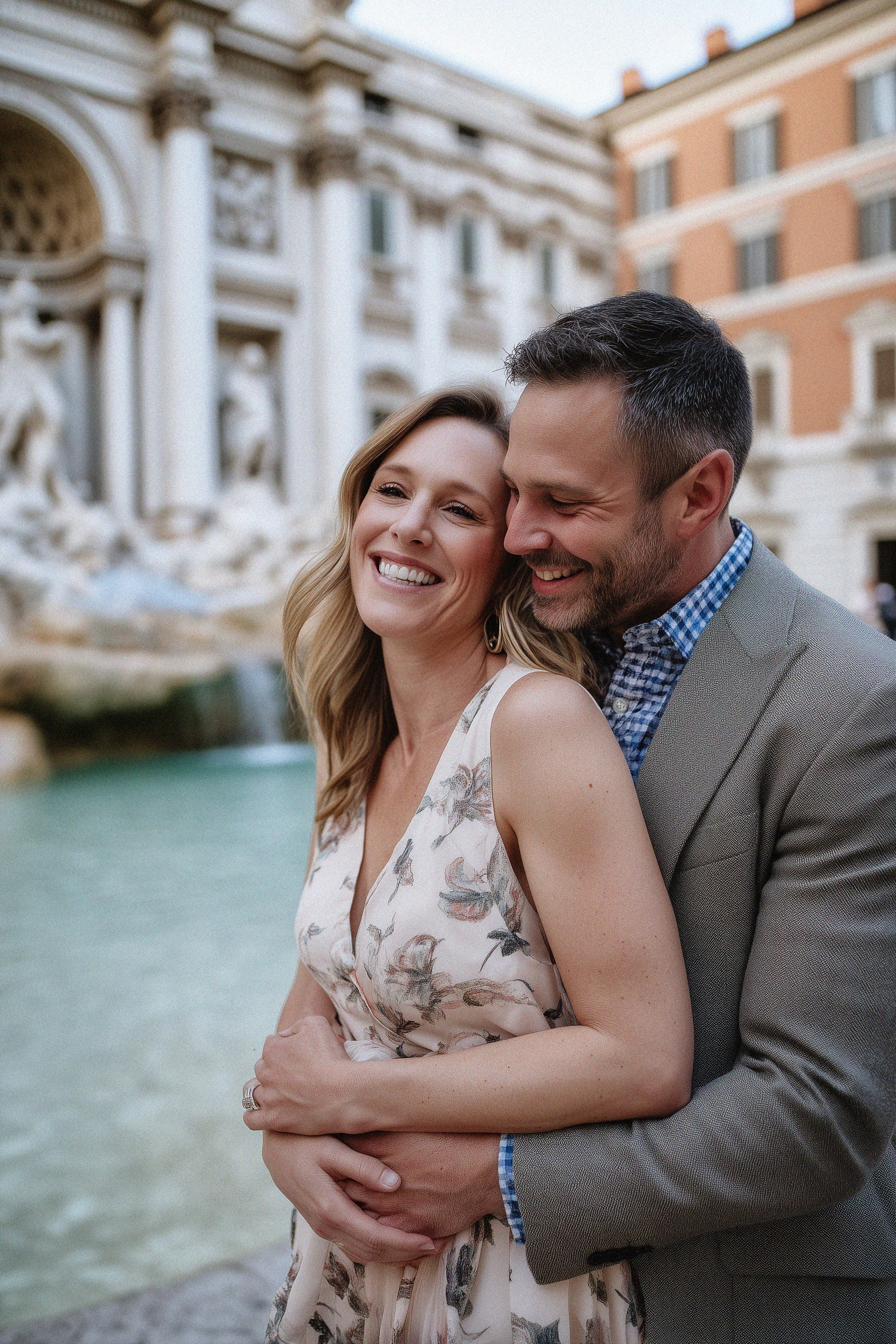 A couple embraces in front of the Trevi Fountain in Rome — the woman smiles joyfully as her partner holds her close.