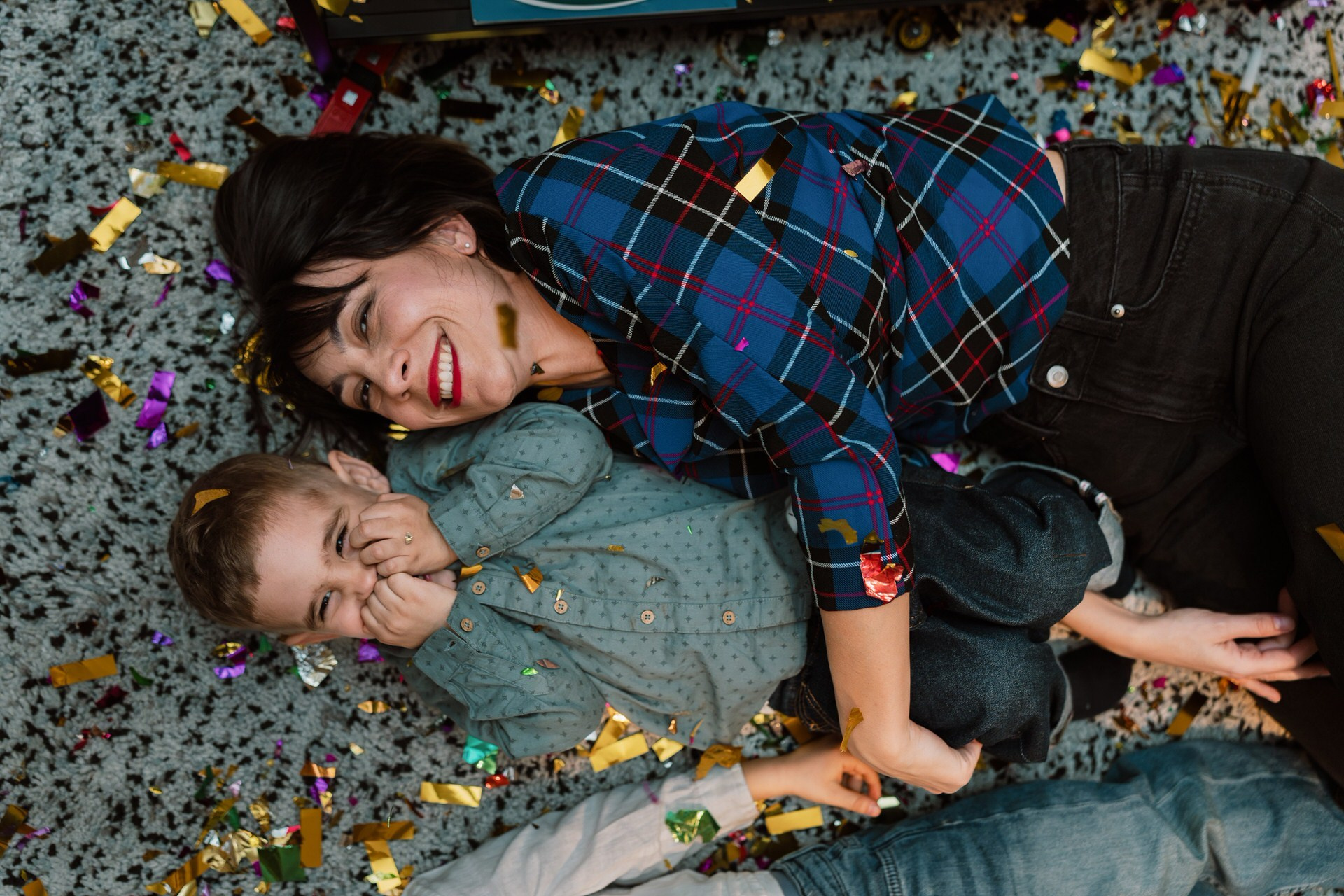 mama i dečak leže na tepihu prekrivenom konfetama za rođendan