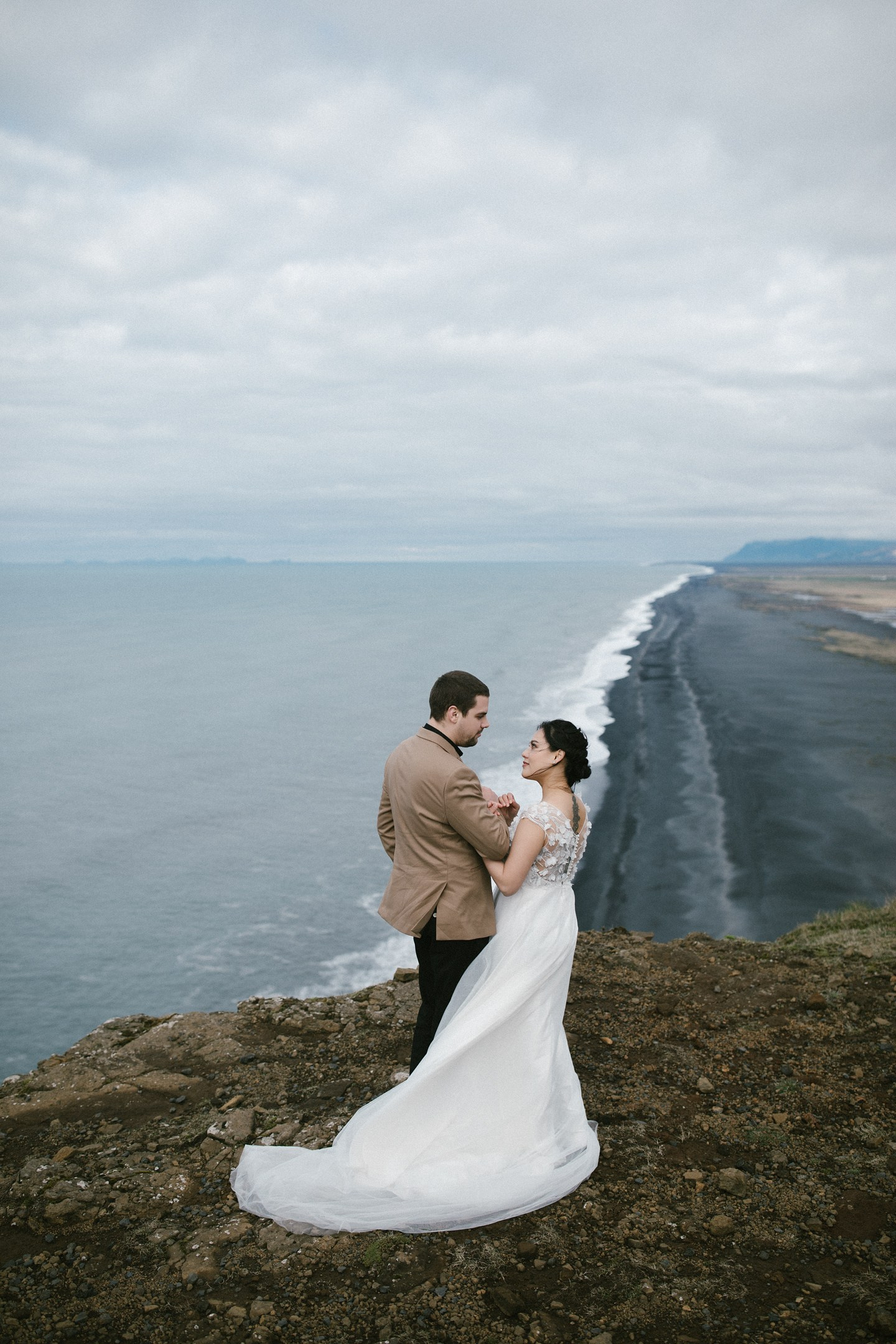 Couple on cliff overlooking Iceland’s dramatic black coastline