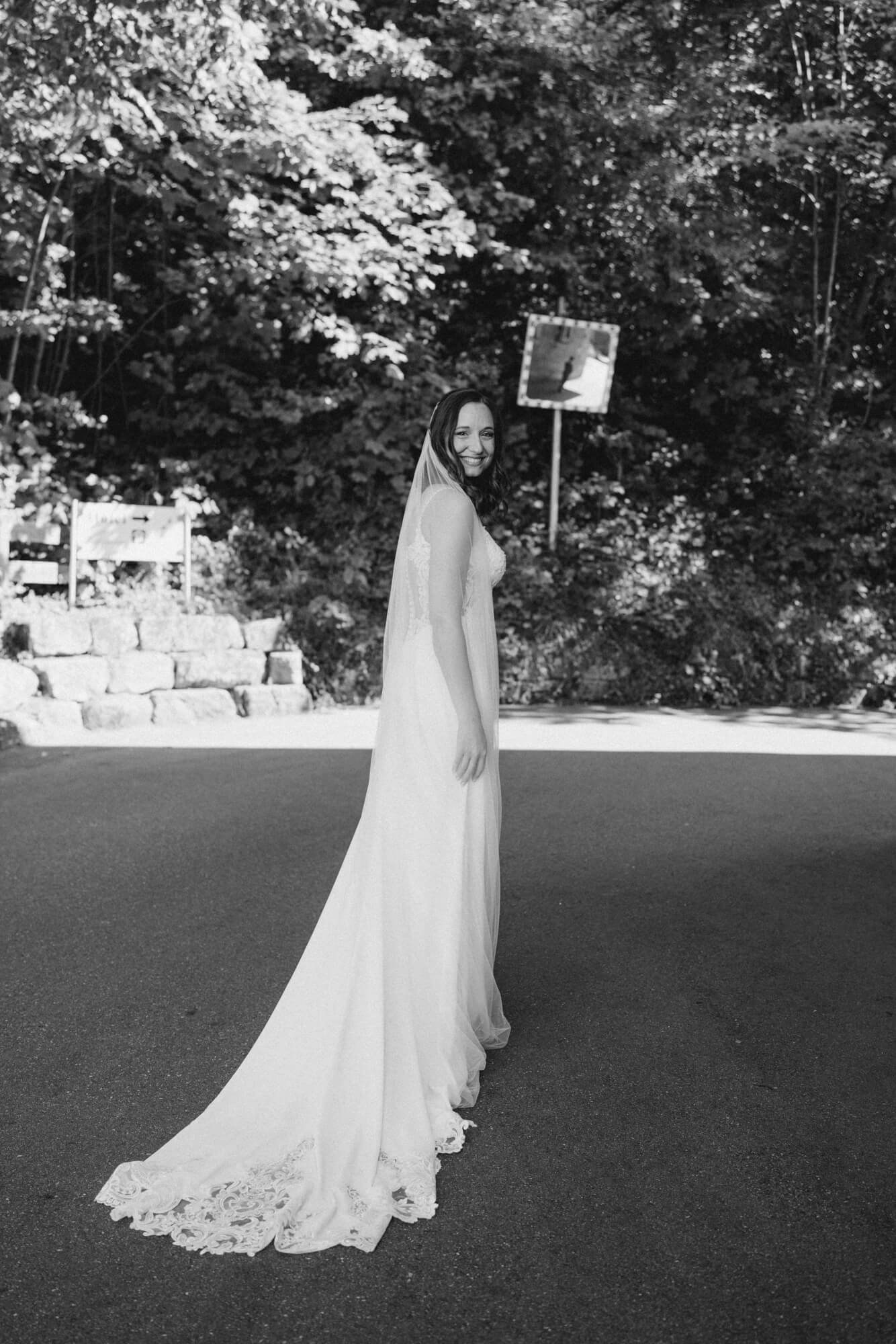 Bride seen from behind, her cathedral-length veil and lace-trimmed gown train fanning wide as she looks over her shoulder; black and white