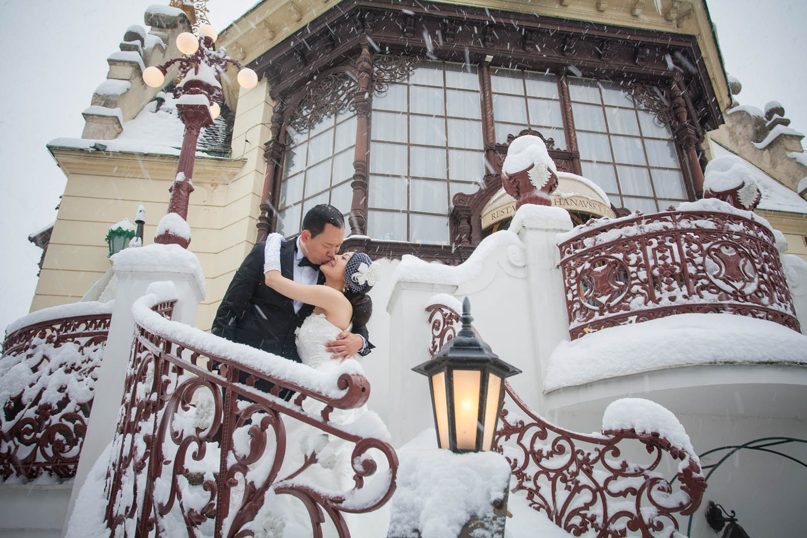 Couple embracing on snowy riverside with Prague Castle view in the background, winter engagement Prague.