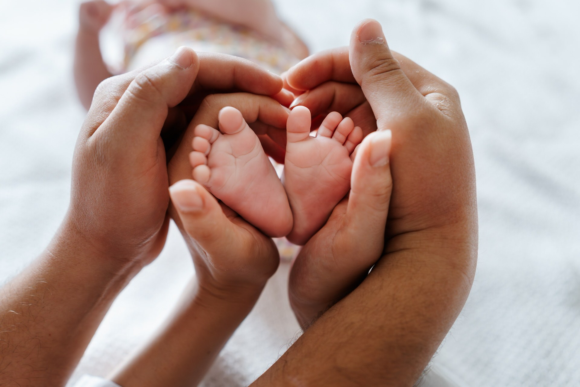 Malena stopala novorođenčeta u rukama njenih roditelja.