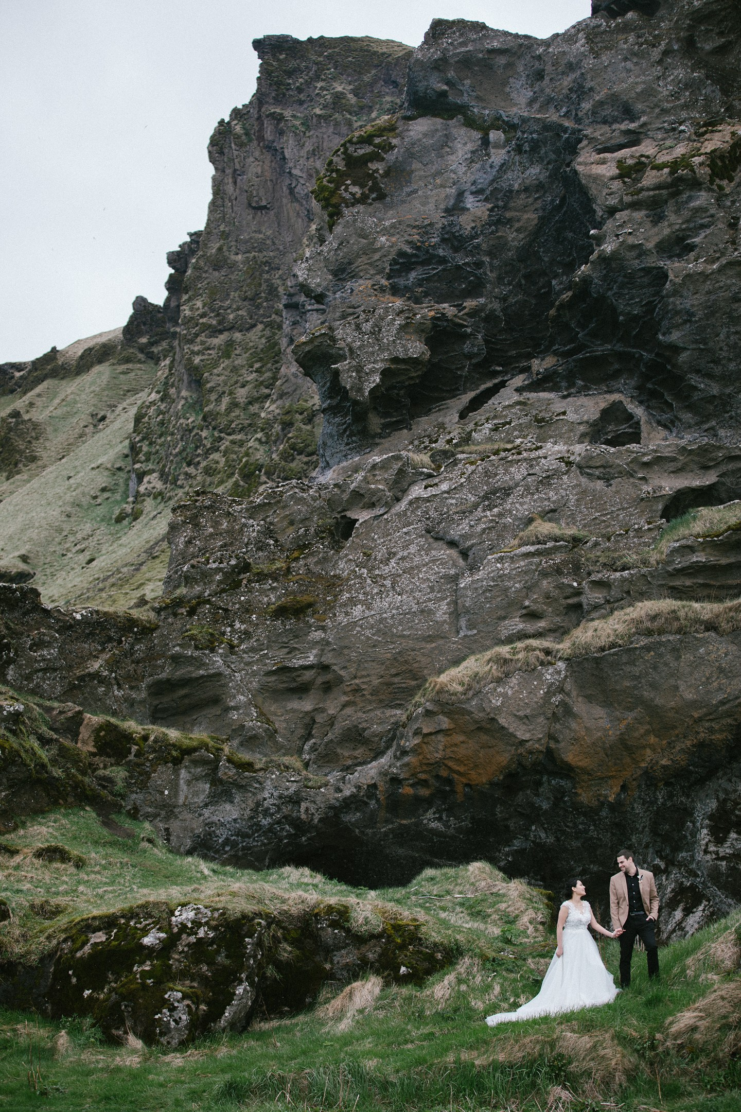 Couple beneath towering cliff – bold and wild Icelandic backdrop