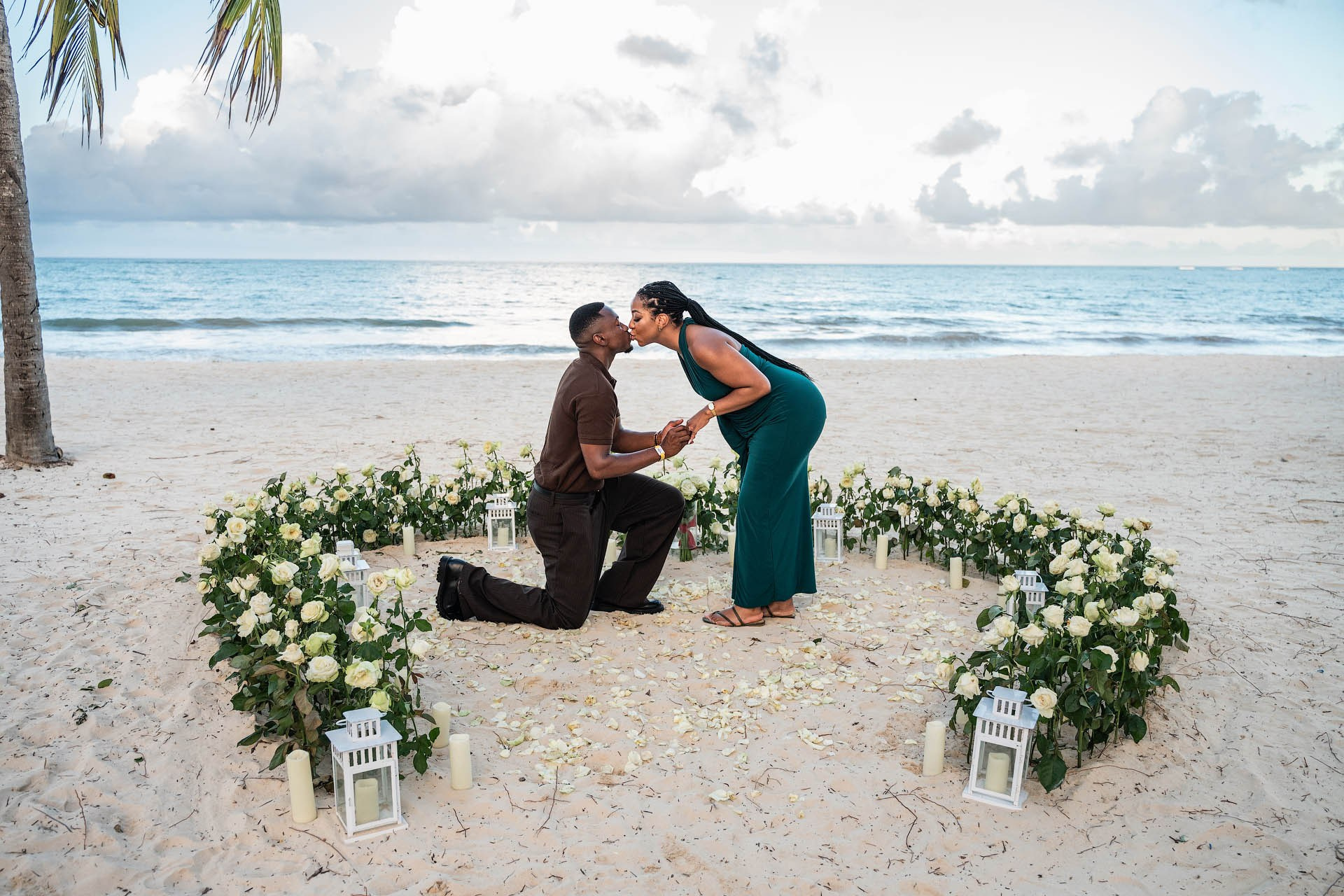 Couple kissing on the beach inside a large white rose heart surrounded by candles and lanterns.