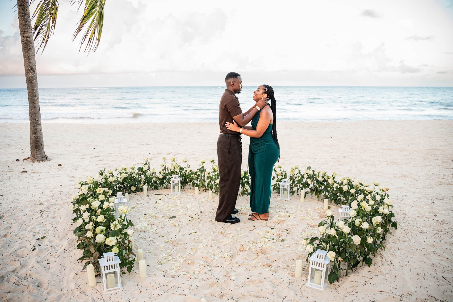 Newly engaged couple holding each other on Arena Gorda Beach inside a heart-shaped arrangement of white roses.