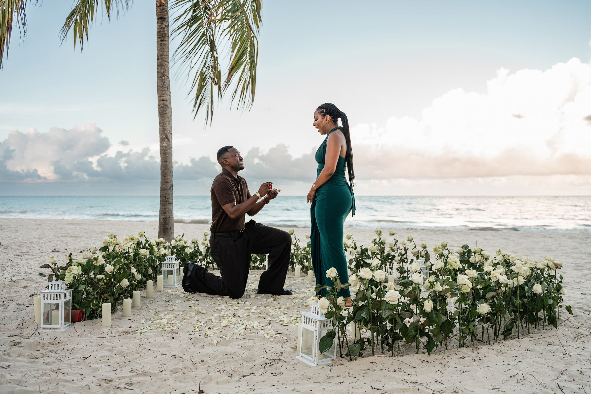 Man kneeling with an engagement ring inside a large heart of fresh white roses on Arena Gorda Beach in Punta Cana.