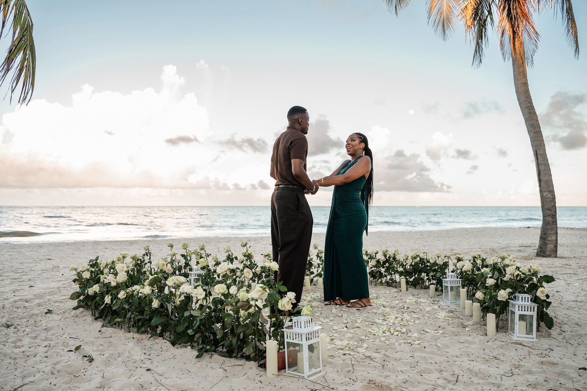 Couple holding hands inside a romantic heart made of fresh white roses, with the Caribbean beach behind them.