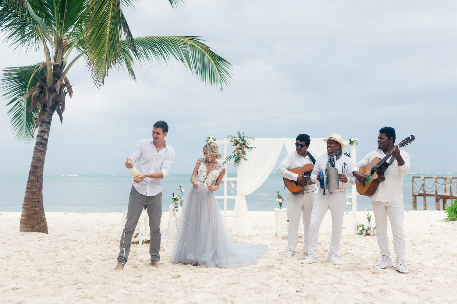 Жених с невестой открывают бутылку шампанского под звуки живой музыки.