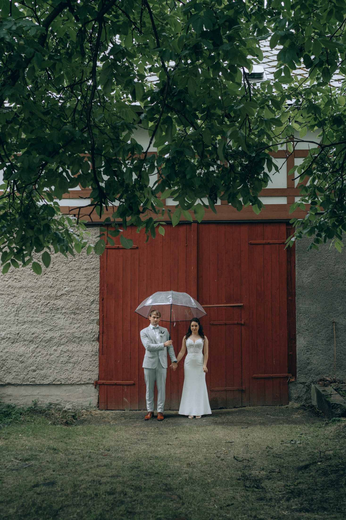 Brautpaar mit Regenschirm vor rotem Tor – kreative Hochzeitsreportage Sachsen