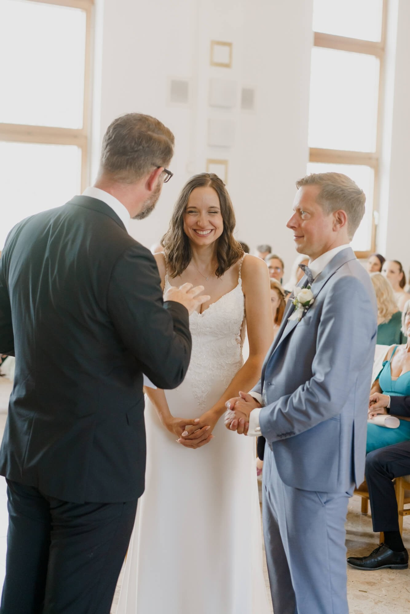 Couple standing together at the altar with an officiant during the wedding ceremony, the bride smiling toward the groom