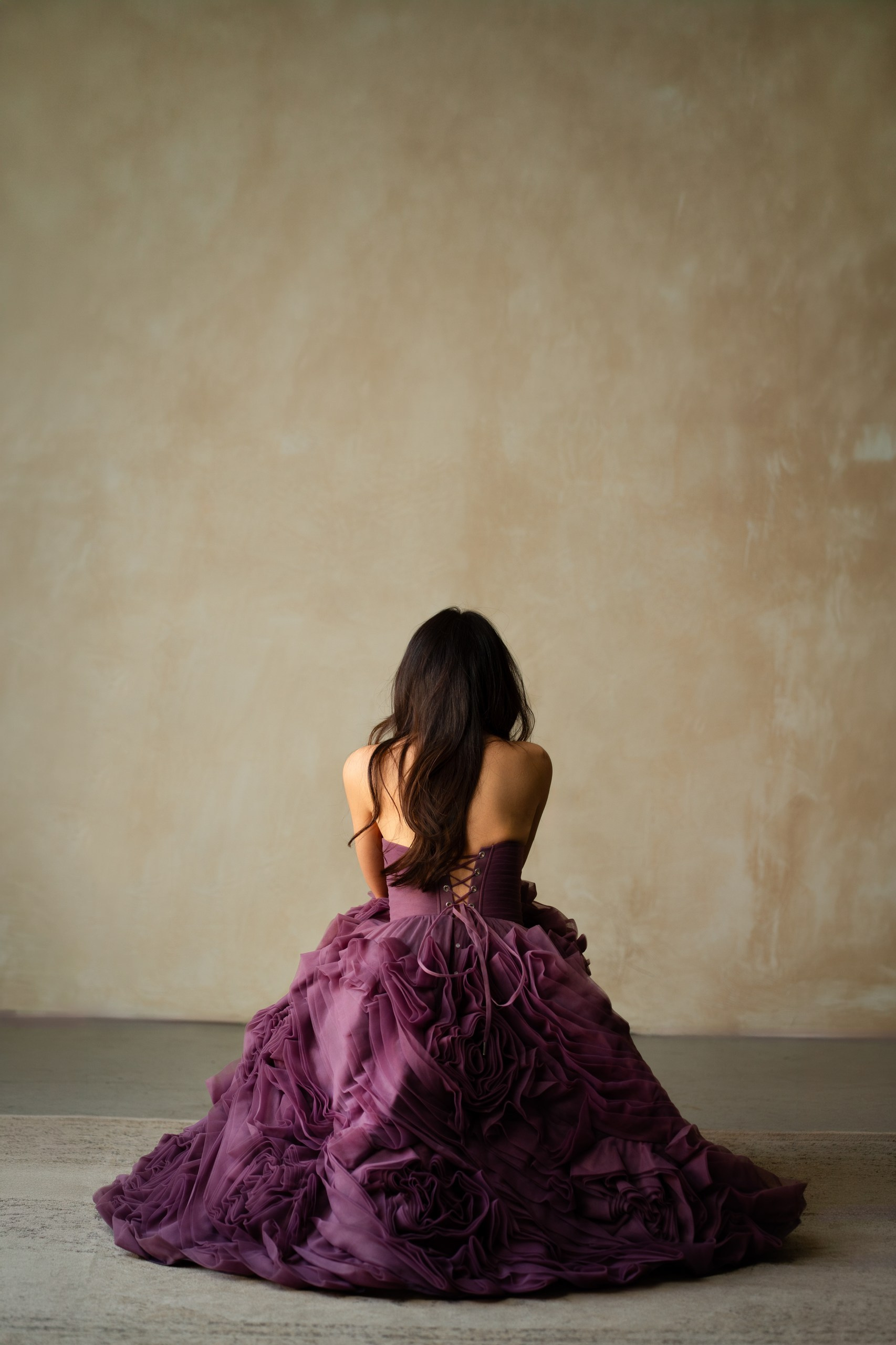 devojka okrenuta leđima u ljubičastoj haljini sedi na podu 