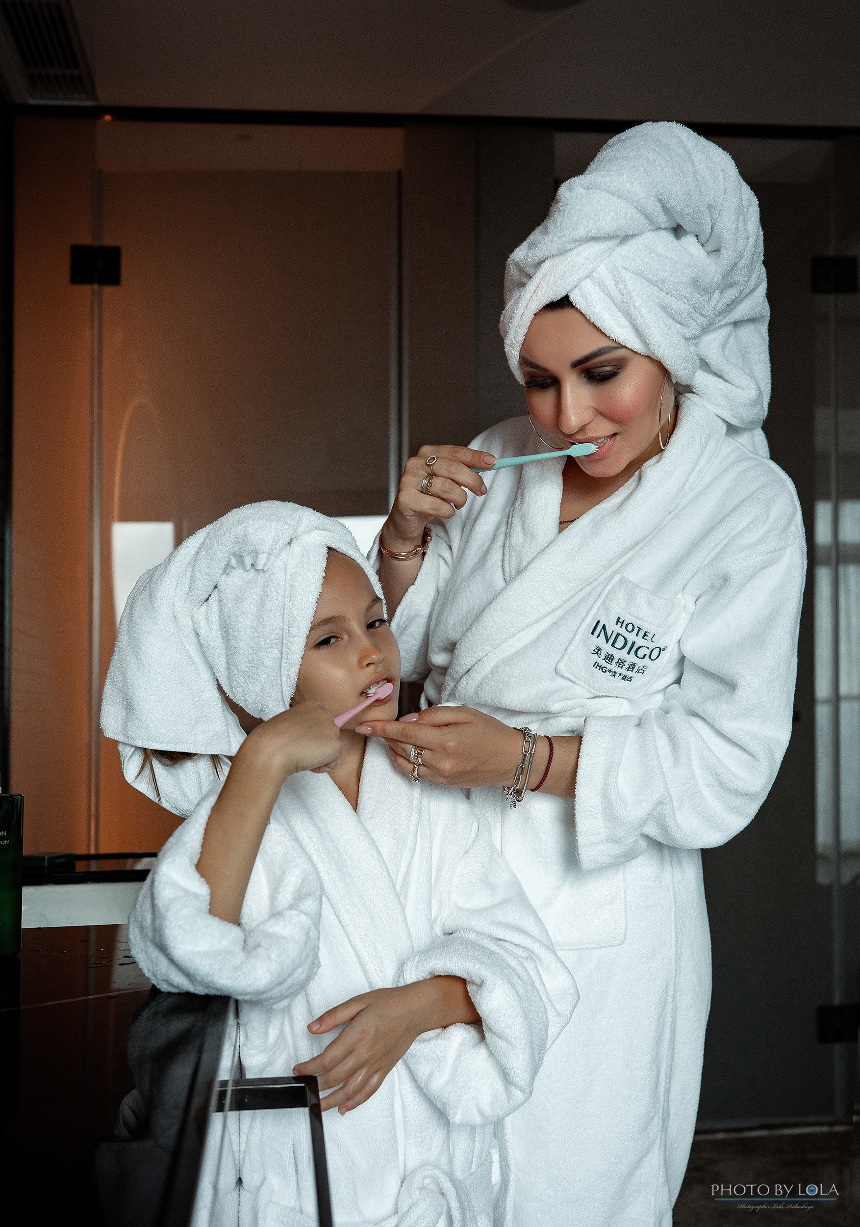 Photo session for mom and daughter. Shooting in a hotel room. Mom and daughter in white robes brushing teeth in the morning.