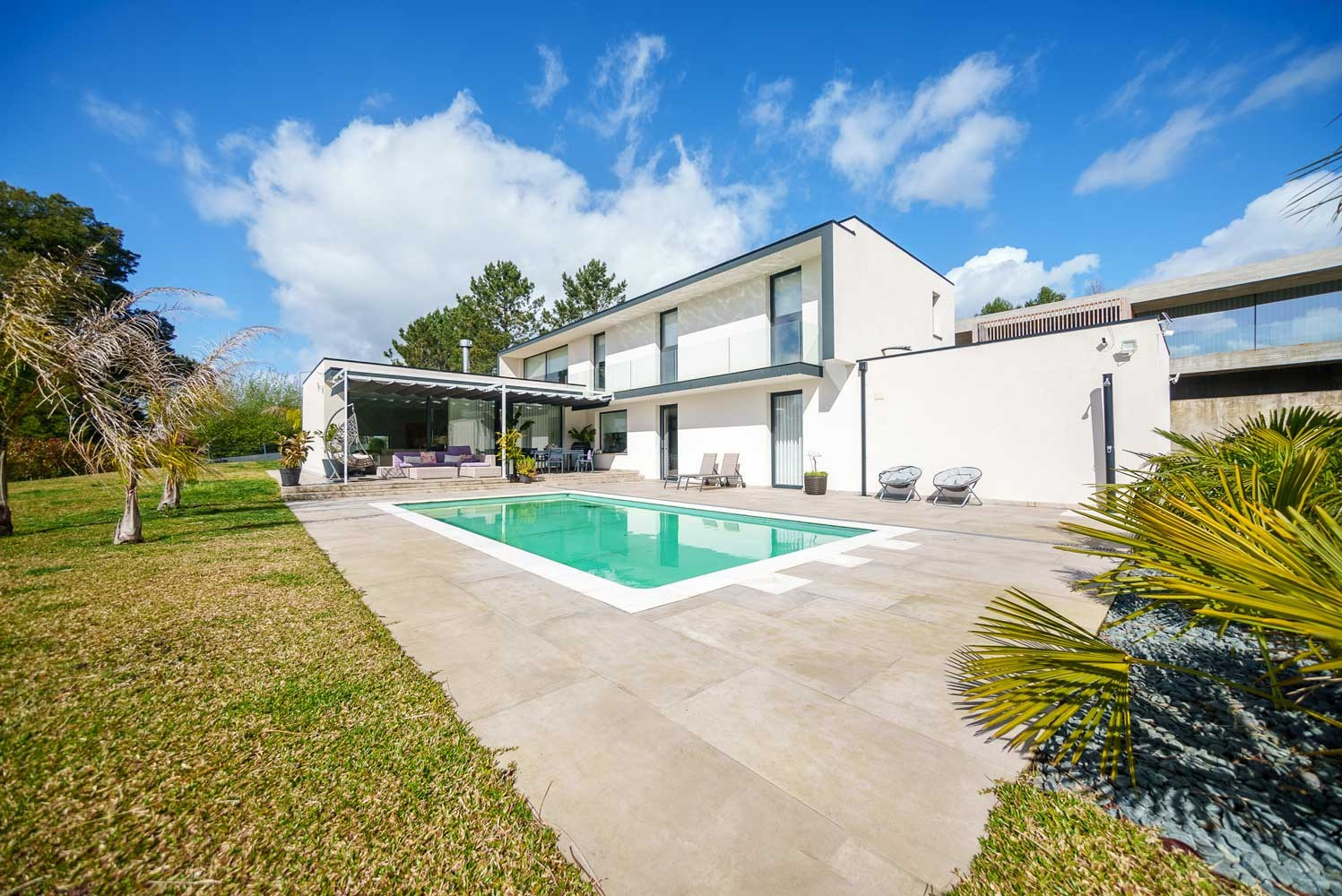 Fotografia de arquitetura e imobiliário exterior de uma casa moderna branca com piscina e jardim sob céu azul, captada pela Khave Media