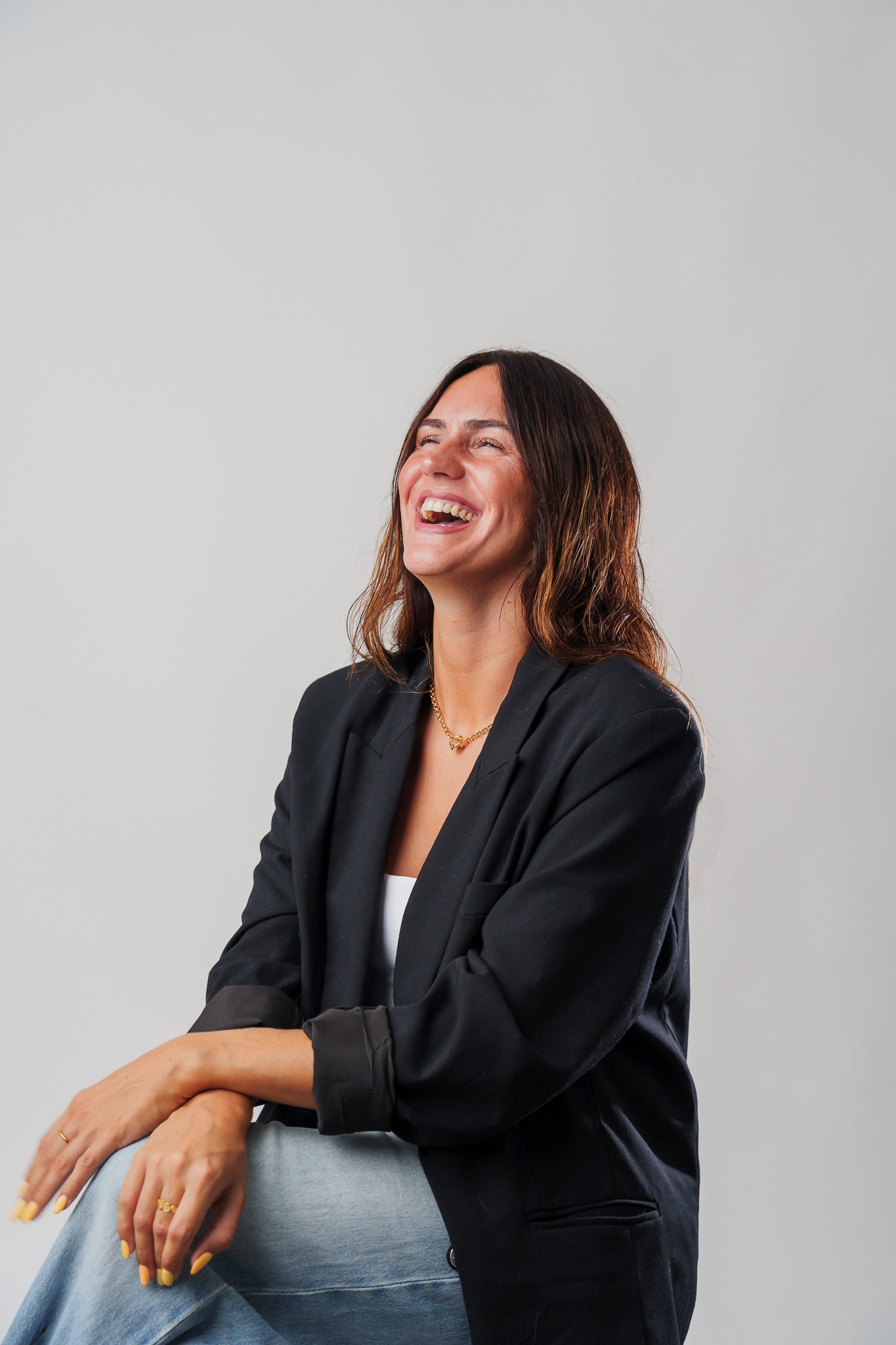 Fotografia de retrato profissional em estúdio de uma mulher a rir com um blazer preto contra um fundo cinzento claro