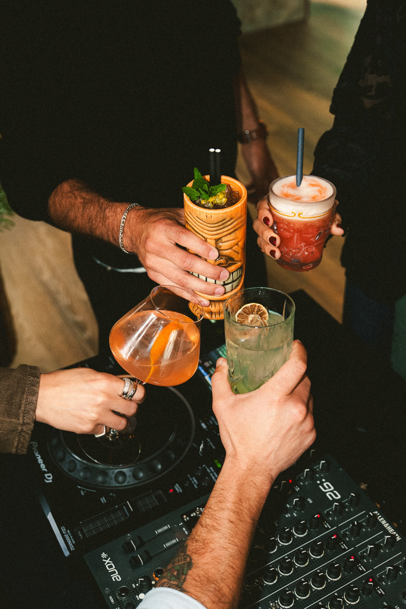 Fotografia de eventos e vida noturna com um plano aproximado de várias mãos a brindar com cocktails coloridos num ambiente de bar