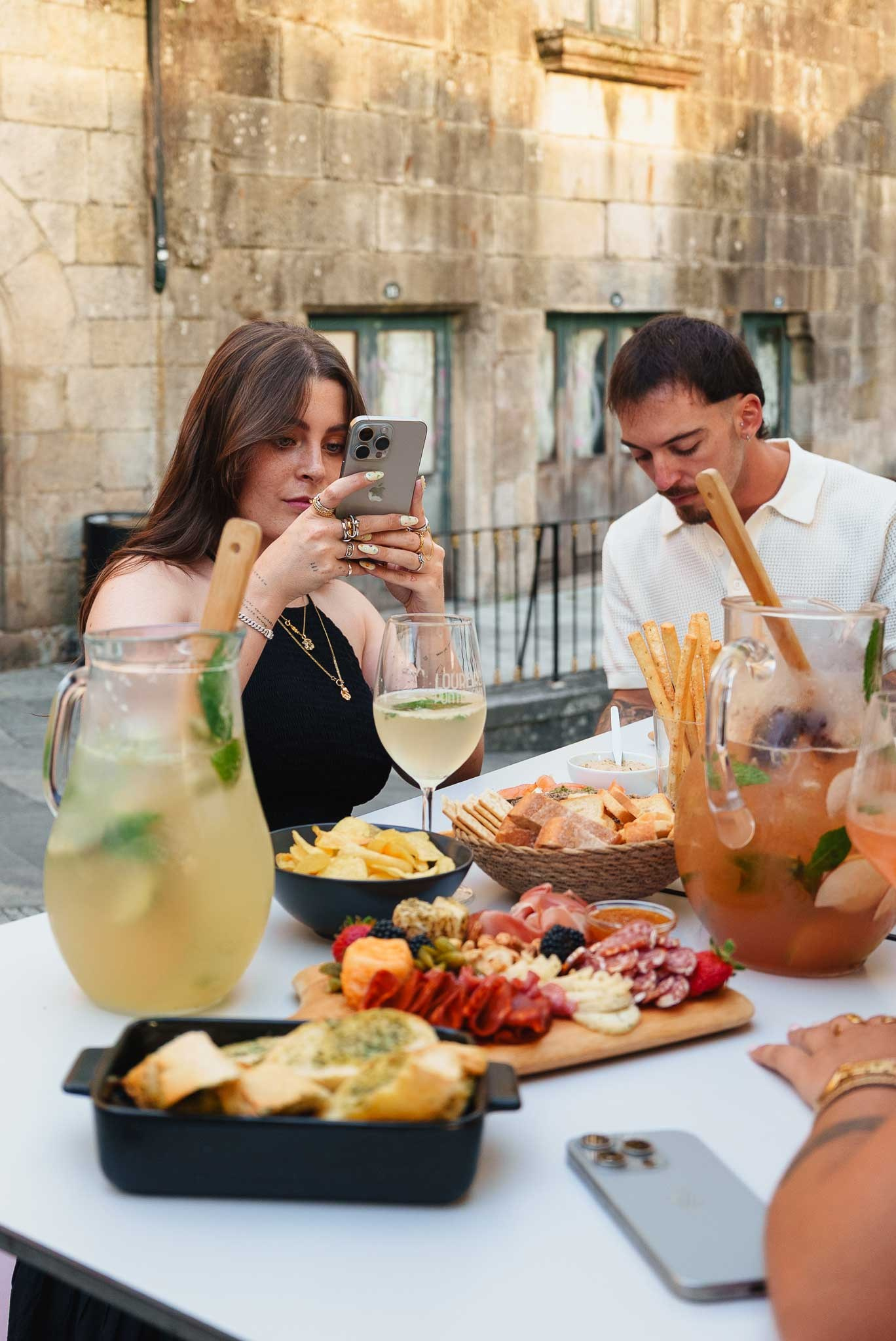 Fotografia lifestyle de um momento de convívio com pessoas numa esplanada a desfrutar de uma tábua de charcutaria e bebidas ao sol