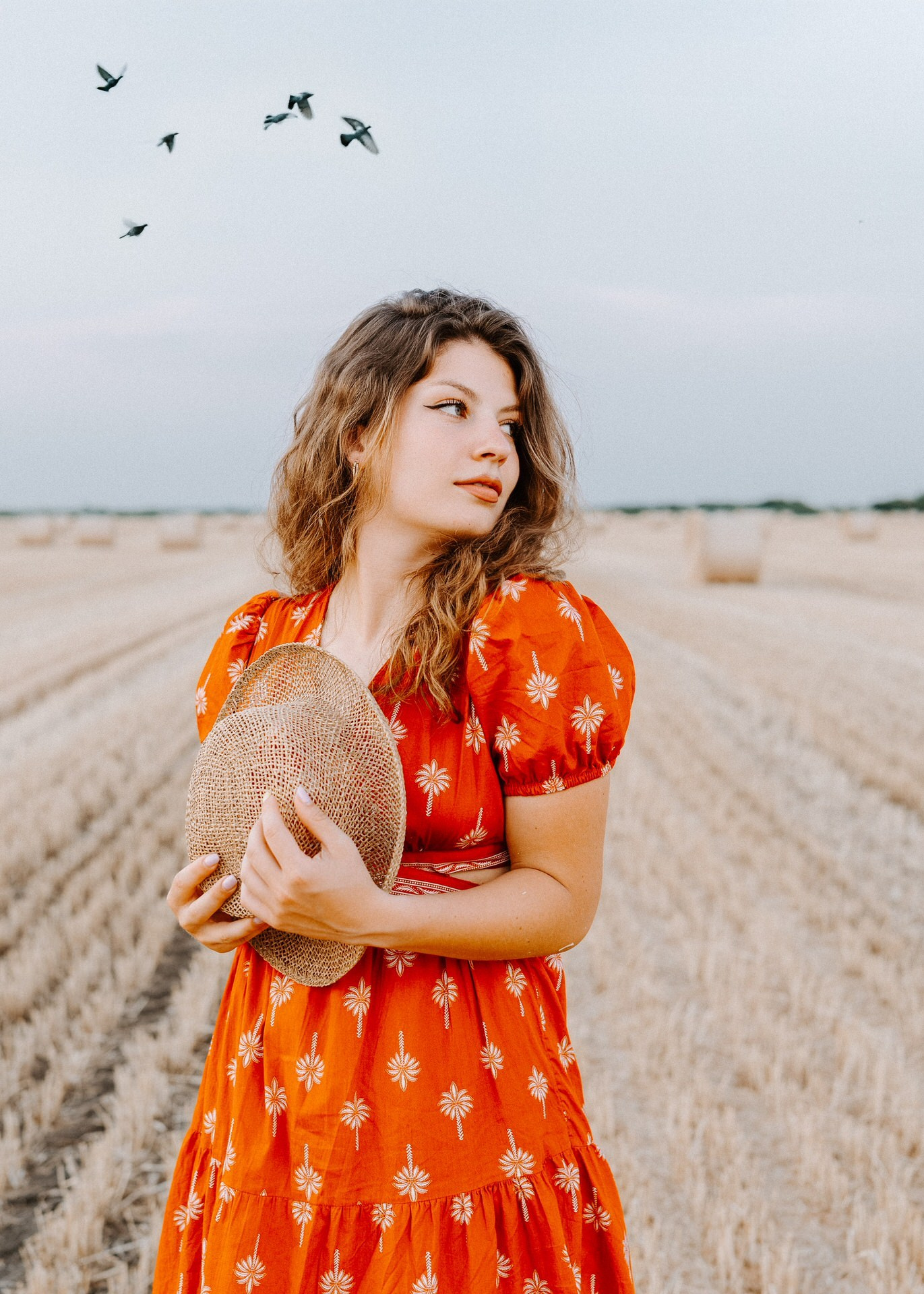 portret devojke na njivi koja gleda u stranu, pticeu pozadini